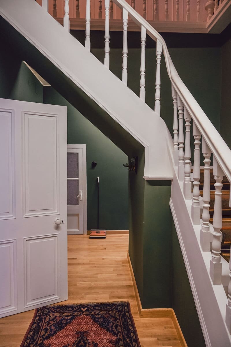 Hallway with deep green walls and a white painted staircase