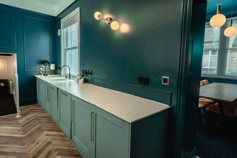 Kitchen colour-drenched in deep teal, with a sash window and herringbone floor