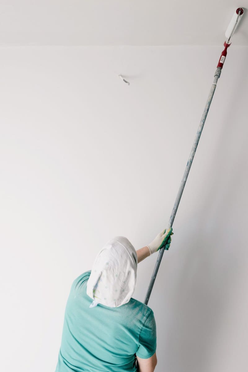 Decorator painting a ceiling with an extension roller