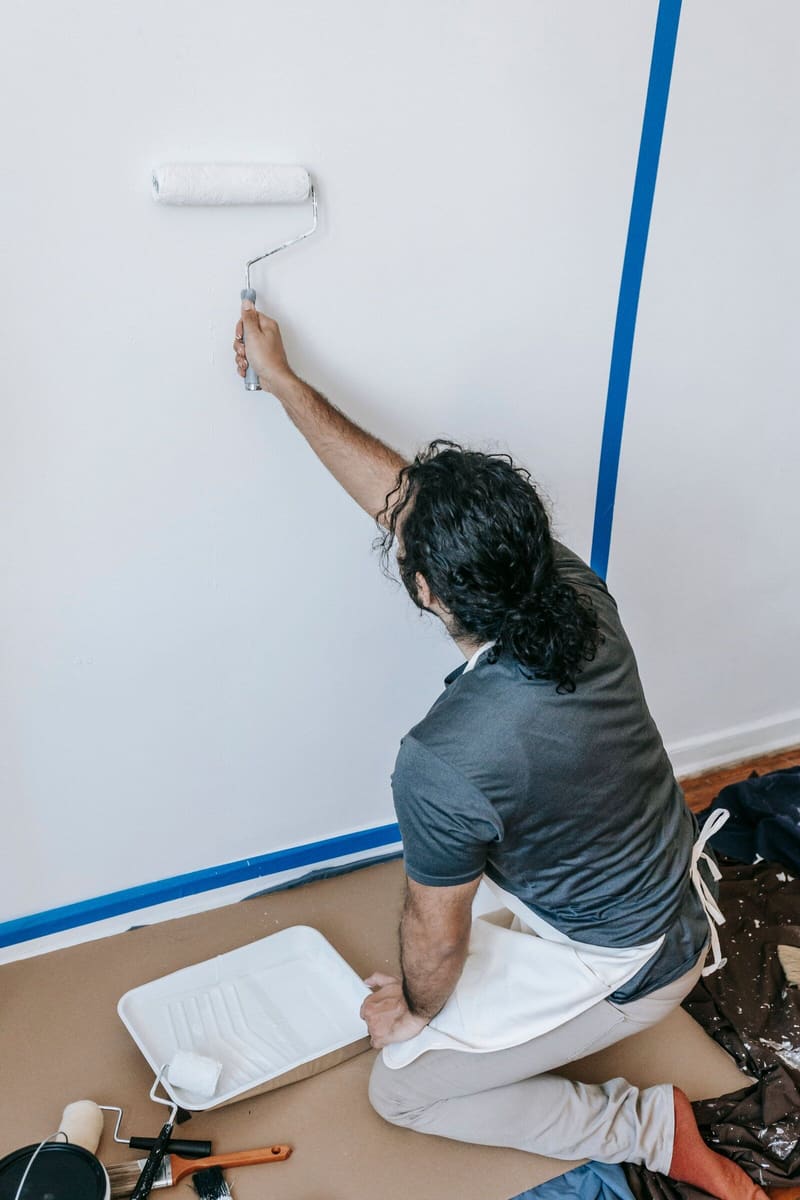 Decorator rolling white paint beside a masked blue tape line