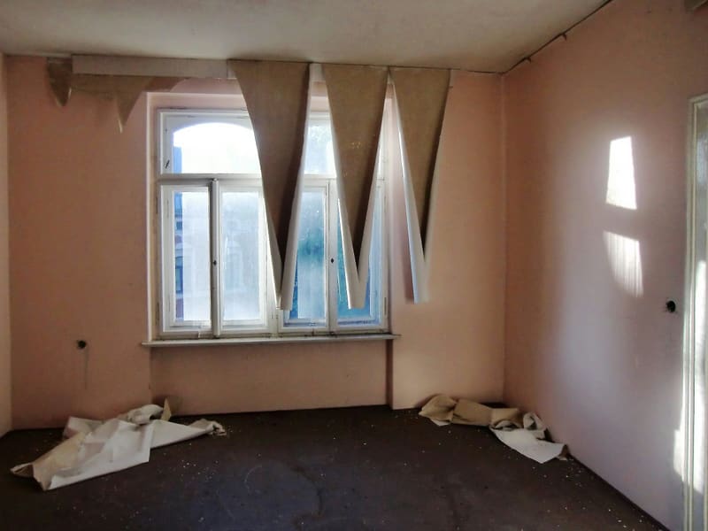 Empty room with old wallpaper peeling off and dust sheets on the floor